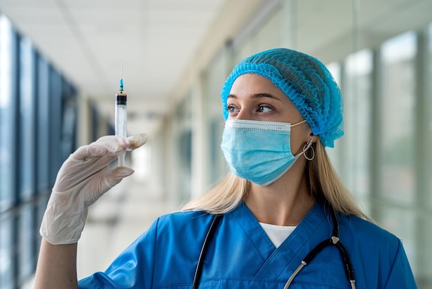 Enfermera joven en uniforme y máscara sosteniendo una jeringa en sus manos en el corredor Concepto de medicina