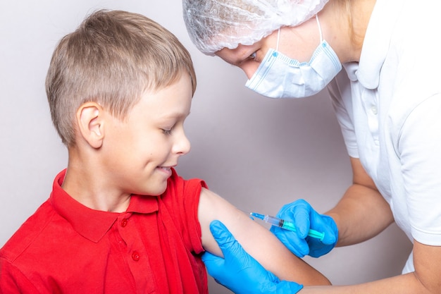 Una enfermera con una máscara y guantes azules inyecta la vacuna a través de una jeringa en un niño.