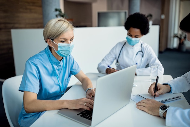 Enfermera con mascarilla protectora trabajando en una laptop en una clínica médica