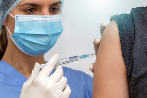 Foto enfermera en mascarilla quirúrgica vacunando a la persona contra los virus