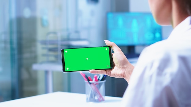 Enfermera médica abriendo la puerta de vidrio del gabinete del hospital y el médico con teléfono inteligente con pantalla verde. Especialista en salud en gabinete de hospital con teléfono inteligente con maqueta.