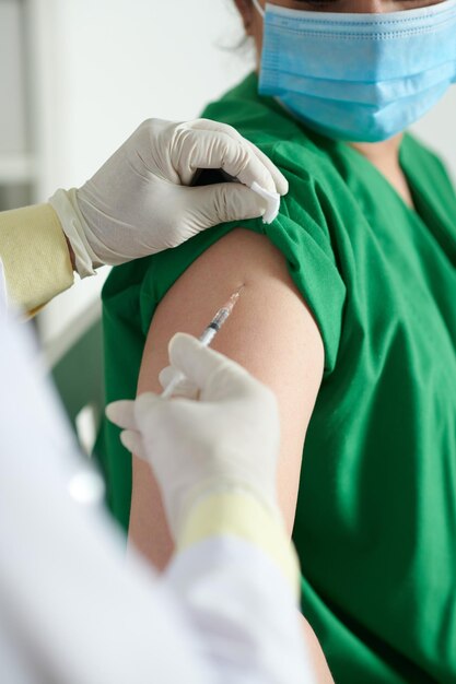 Enfermera médica en batas y guantes protectores recibiendo la vacuna contra el coronavirus en el hombro
