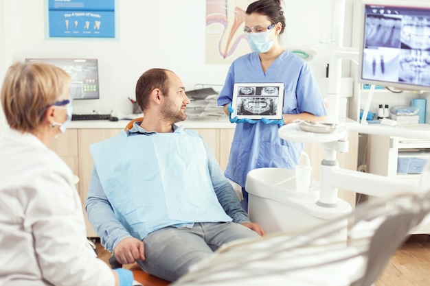 Enfermera médica que muestra en la radiografía de los dientes de la tableta que lo muestra con el paciente