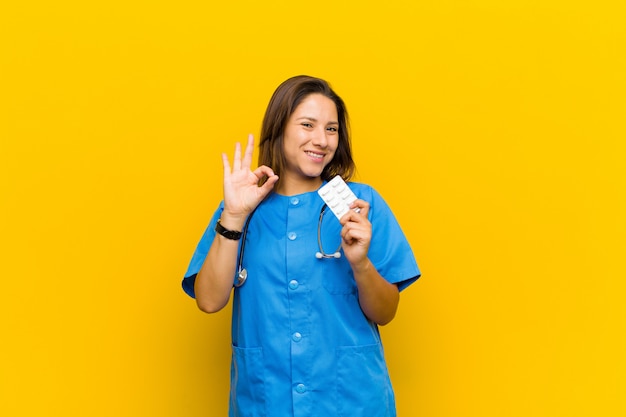 Enfermera mujer con pils contra la pared naranja