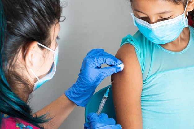 Foto enfermera de niños limpiando la sangre con algodón después de administrar la inyección en el brazo de una niña marrón