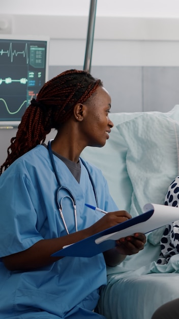 Enfermera pediatra afroamericana escribiendo tratamiento sanitario durante el examen de recuperación