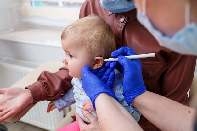 Una enfermera perfora las orejas de una niña de ocho meses. Belleza para niños pequeños