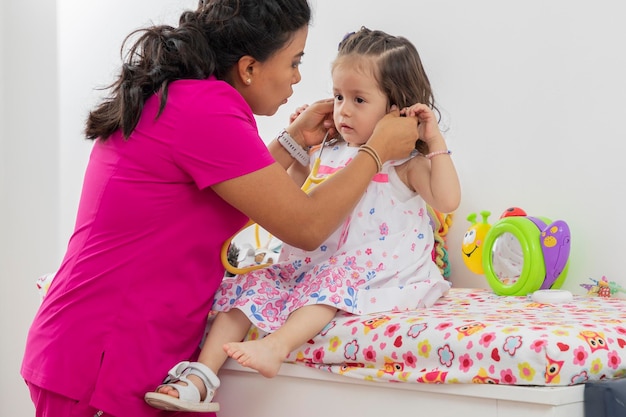 Enfermera poniéndole un estetoscopio a una niña para que pueda jugar con él