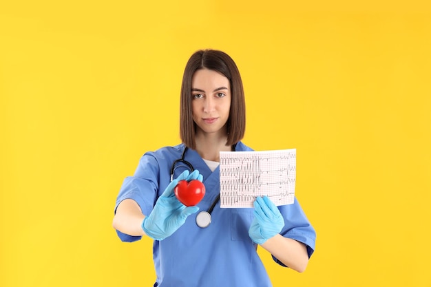 Enfermera en prácticas con corazón y ecg sobre fondo amarillo