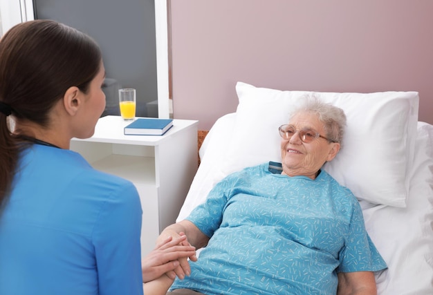 Enfermera que ayuda a la anciana acostada en la cama en la sala del hospital