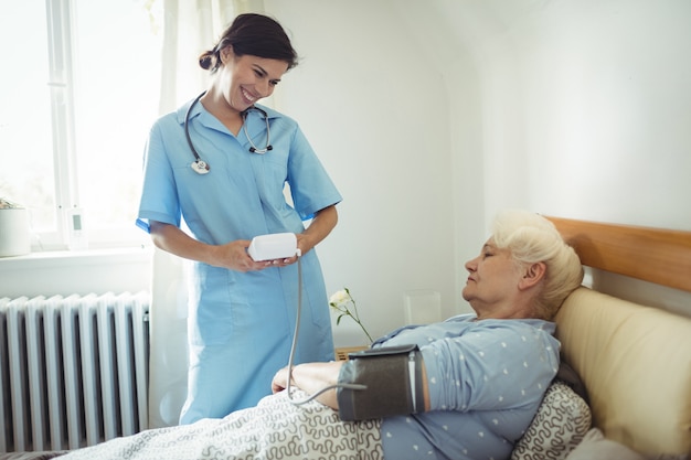 Enfermera que controla la presión arterial de la mujer mayor