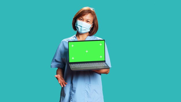 Enfermera que muestra un video informativo del procedimiento médico en una computadora portátil simulando la pantalla verde de la clave cromática. Empleado del hospital presentando cinta explicativa de atención médica, aislada sobre fondo azul del estudio