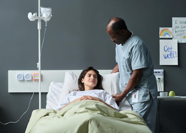 Enfermera que se preocupa por el paciente enfermo mientras está acostada en la sala del hospital