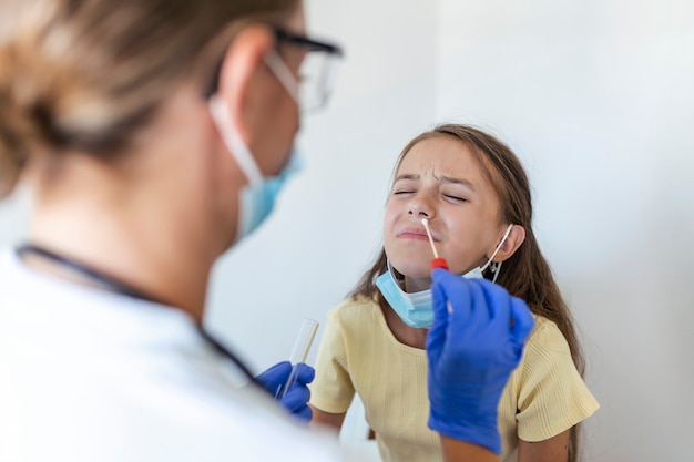 Enfermera realizando una prueba de frotis nasal en un niño pequeño. Niña pasando por una prueba de PCR debido a la pandemia de COVID-19. Doctora con hisopo de algodón mientras prueba de PCR niña pequeña