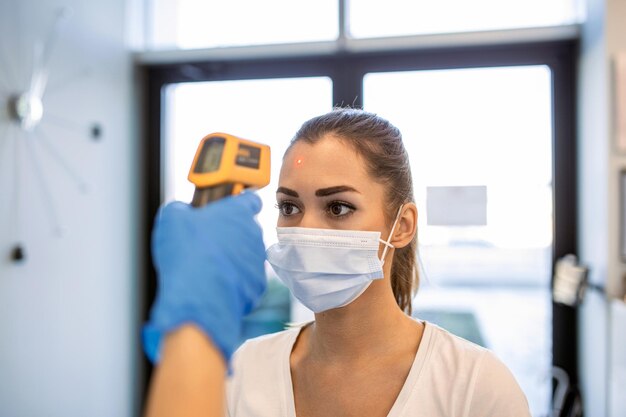 Enfermera revisando la temperatura de la mujer con un termómetro infrarrojo en el mostrador La mujer lleva una mascarilla protectora Están en el hospital durante la pandemia