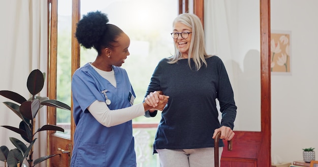 Enfermera senior y ayuda con bastón para la rehabilitación bienestar y hablar con sonrisa cuidador africano paciente feliz y anciano con discapacidad bastón y apoyo para la recuperación