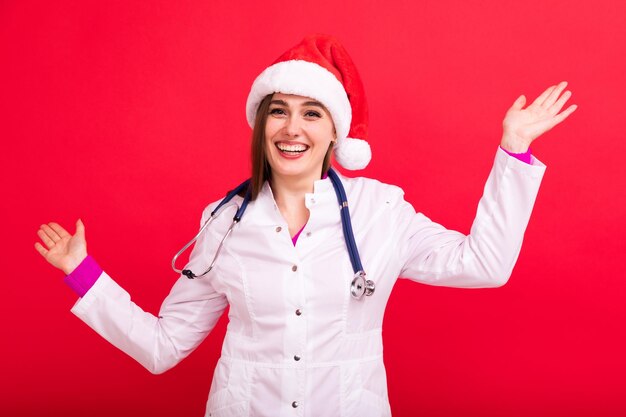 Una enfermera con un sombrero de Papá Noel está feliz por el nuevo año con un fondo rojo