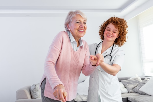 Enfermera sonriente que ayuda a la señora mayor a caminar alrededor del hogar de ancianos.