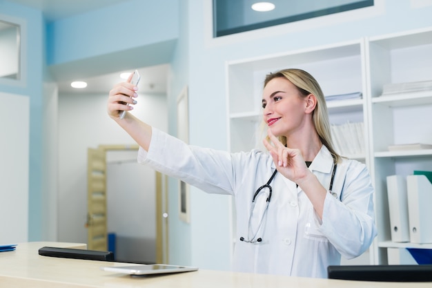 Enfermera sonriente tomando selfies con su teléfono detrás de la recepción