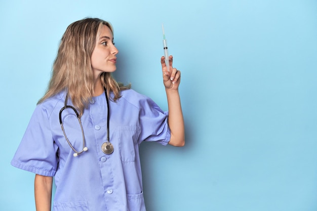 Enfermera sosteniendo aguja para vacunación en estudio azul