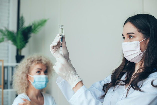 Enfermera sosteniendo la jeringa y haciendo dosis de inyección de vacunación covid usando máscara médica protección contra virus ...