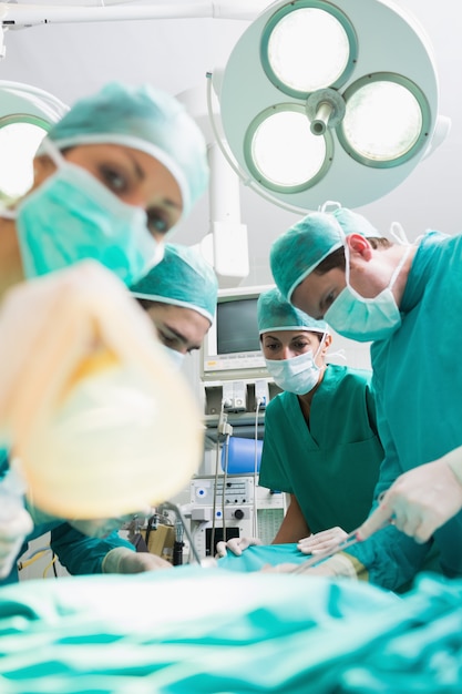 Enfermera sosteniendo una máscara de oxígeno junto a los cirujanos
