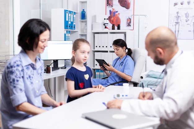 Enfermera con tablet pc mientras el médico consulta a un niño enfermo en la oficina del hospital.