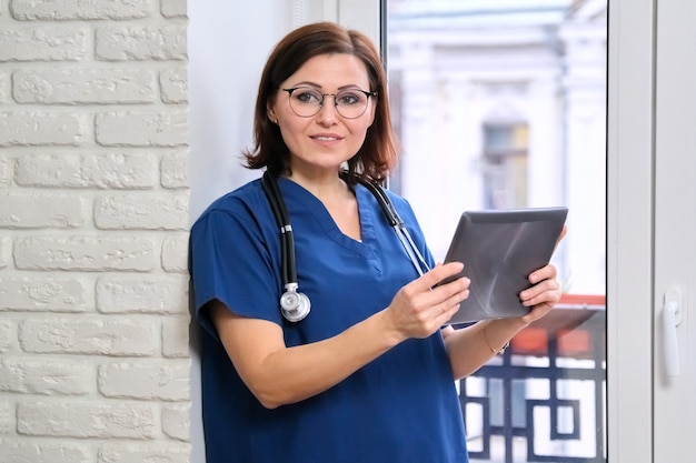 Enfermera con tableta digital, médico junto a la ventana en la oficina de la clínica.