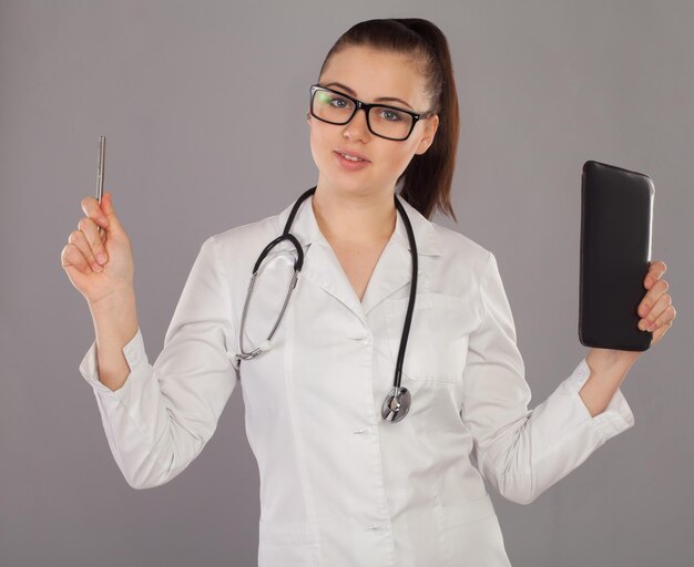 La enfermera con túnica blanca y anteojos negros está pensando en sus notas sobre un fondo gris