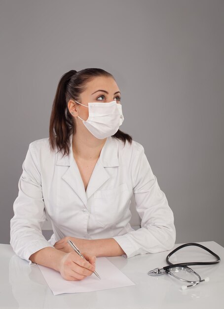 La enfermera con túnica blanca está haciendo un informe en la mesa con un fondo gris