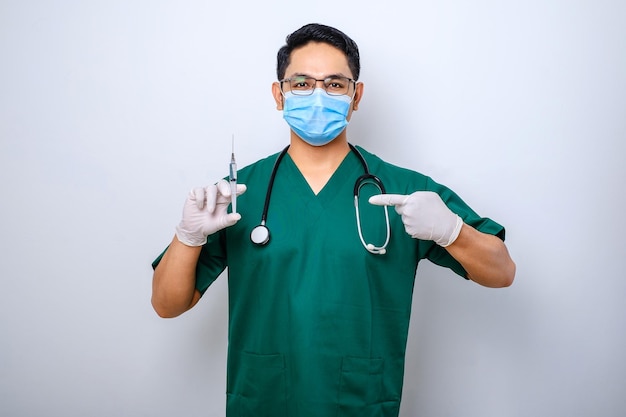 Enfermero o médico serio con mascarilla médica verde apuntando a la jeringa con la vacuna contra el coronavirus