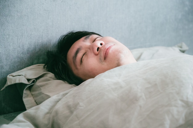 Enfermo asiático macho duerme en la cama. Hombre paciente descansando de la enfermedad.