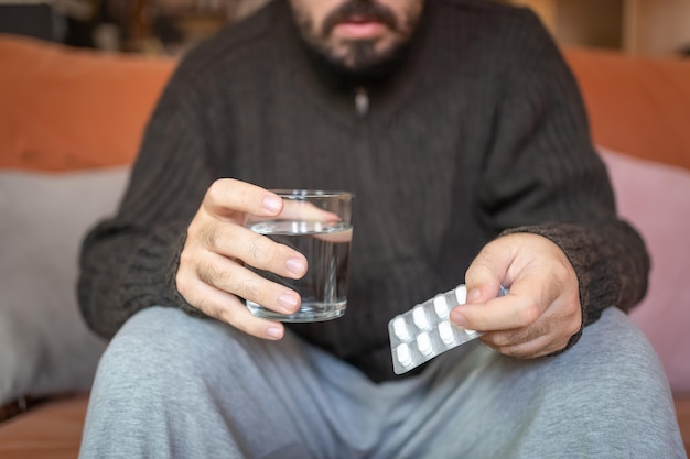 Enfermo sosteniendo un paquete de pastillas y un vaso de agua para beber