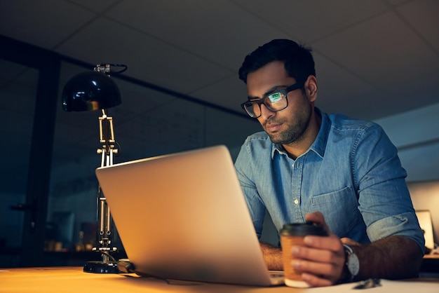 Enfocado en lograr solo la mejor toma recortada de un joven hombre de negocios que trabaja hasta tarde en una computadora portátil en una oficina