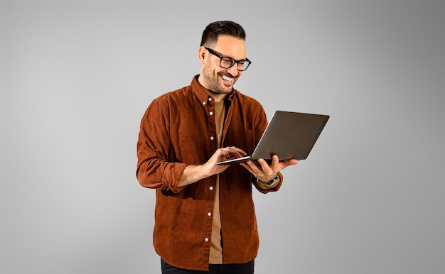 Enfocado sonriente adulto joven apuesto hombre de negocios vestido con camisa trabajando sobre una computadora portátil