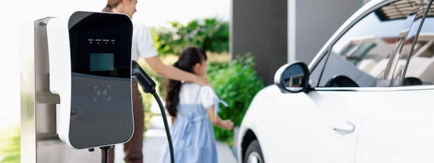 Enfocar el punto de carga EV doméstico progresivo con una mujer y una niña borrosas en el fondo