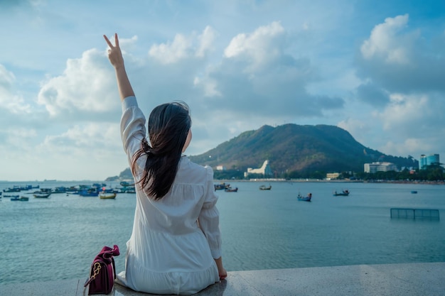 Enfocar la vista posterior de una chica asiática feliz levanta las manos frente a la playa en el concepto de Vung Tau Travel