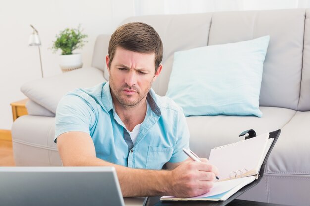 Enfoque hombre mirando es portátil y escribir en un cuaderno