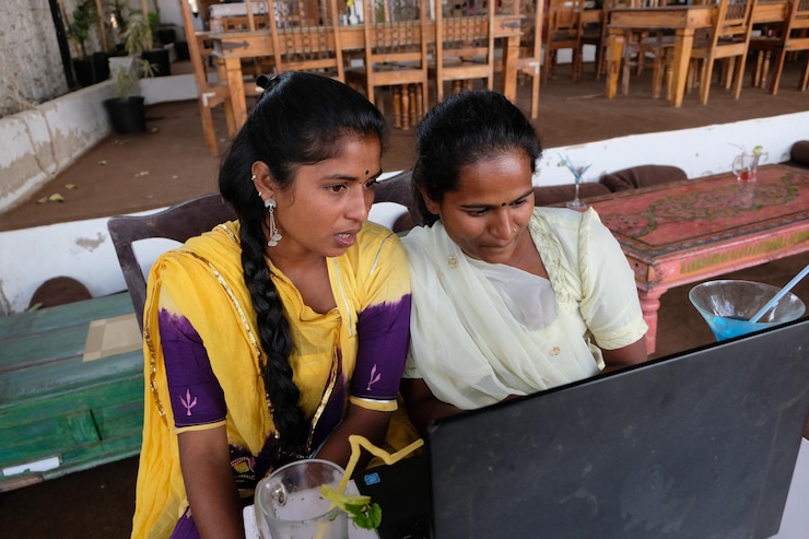 Foto enfoque poco profundo de dos mujeres indias mirando una laptop con vasos de bebidas en una mesa