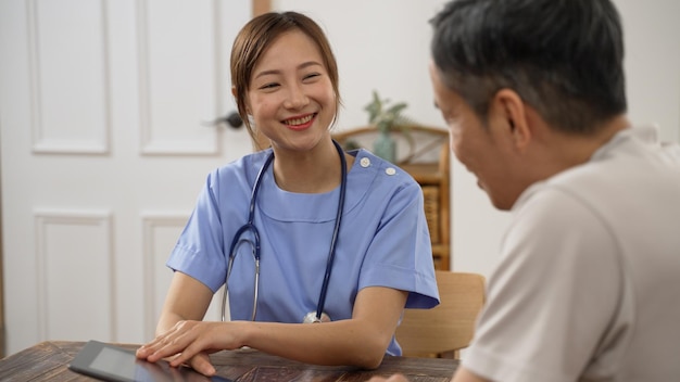 enfoque selectivo de una amigable doctora asiática que consulta a un paciente maduro con una almohadilla electrónica mientras visita su casa.