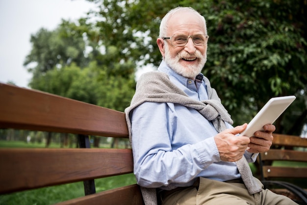Enfoque selectivo de un anciano sonriente que usa una tableta digital mientras se sienta en un banco en el parque