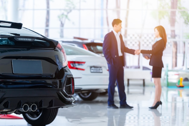 Foto enfoque selectivo en un auto nuevo y difuminar al vendedor profesional del concesionario y a su cliente estrechándole la mano. concepto profesionalismo acuerdo contrato arrendamiento arrendamiento alquiler venta minorista.