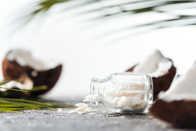 Enfoque selectivo de botella de vidrio con virutas de coco cerca de cocos agrietados y hojas de palma.