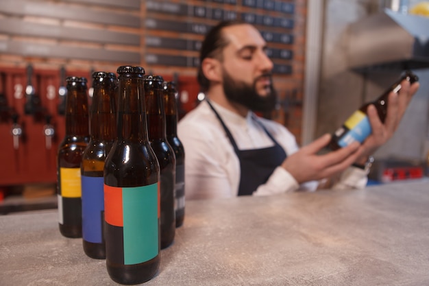 Enfoque selectivo en las botellas de cerveza en el mostrador, barman examinando la botella de cerveza