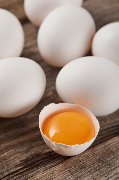 Enfoque selectivo de la cáscara de huevo rota con yema amarilla cerca de los huevos en la mesa de madera.