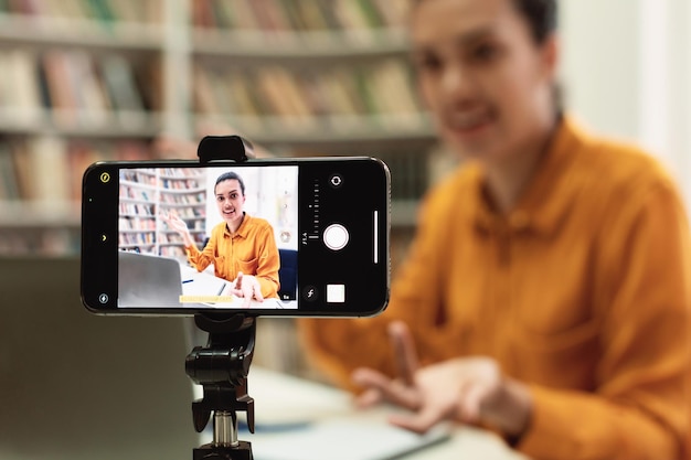 Enfoque selectivo en el conjunto de teléfonos inteligentes en trípode profesora o conferenciante que transmite desde la biblioteca que graba la lección en línea