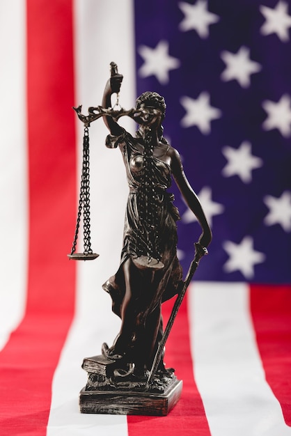 Foto enfoque selectivo de la estatua de la justicia cerca de la bandera americana con estrellas y rayas.
