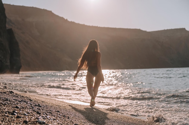 Enfoque selectivo Feliz mujer sensual despreocupada con cabello largo en traje de baño negro posando en la playa al atardecer Silueta de joven hermosa mujer positiva juguetona al aire libre Vacaciones de verano y concepto de viaje