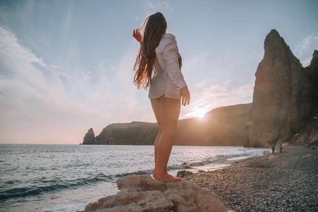 Enfoque selectivo feliz mujer sensual despreocupada con cabello largo en traje de baño negro posando en la playa al atardecer