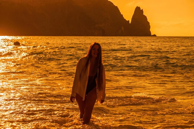 Enfoque selectivo feliz mujer sensual despreocupada con cabello largo en traje de baño negro posando en la playa al atardecer